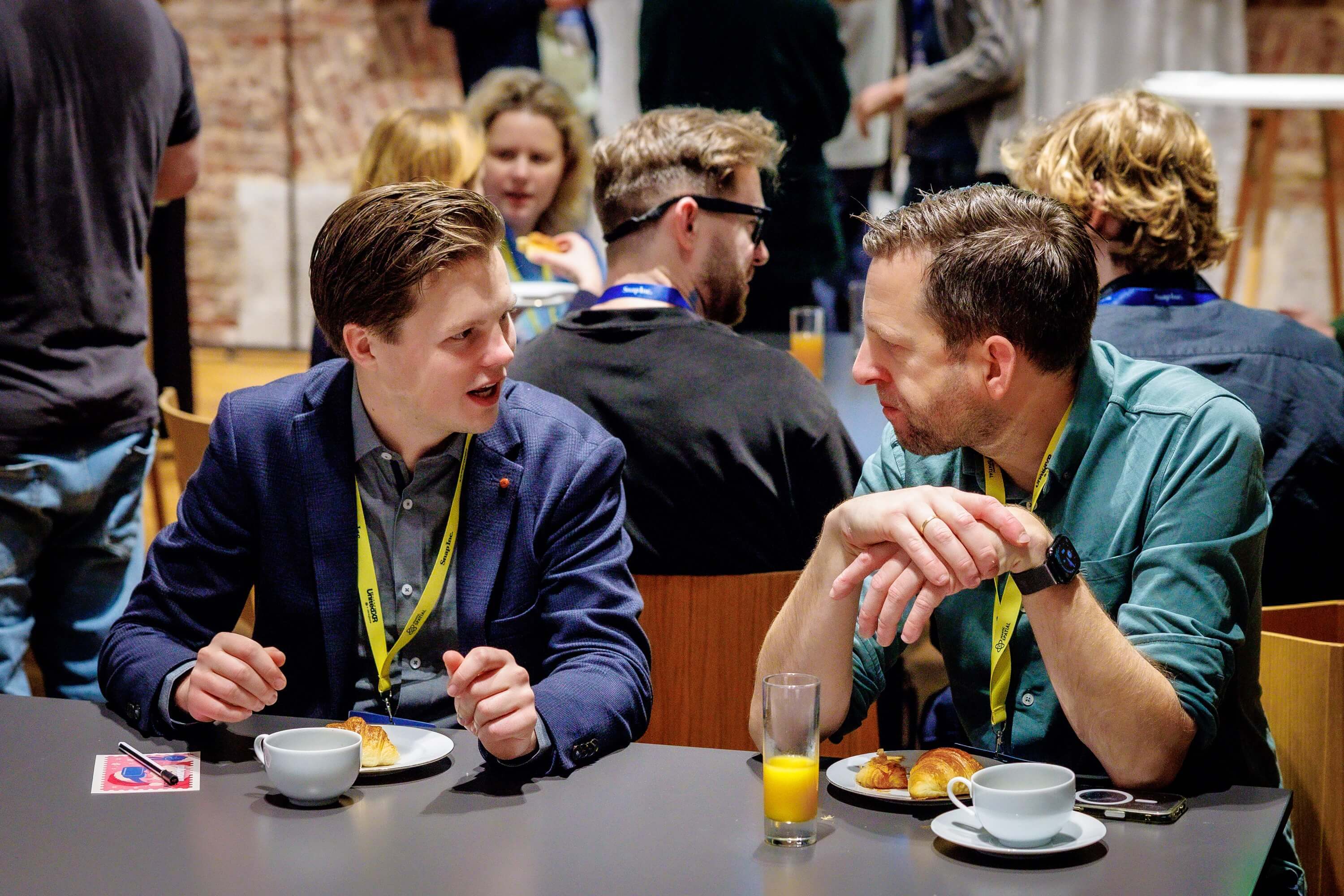 twee mensen in gesprek met andere mensen op de achtergrond