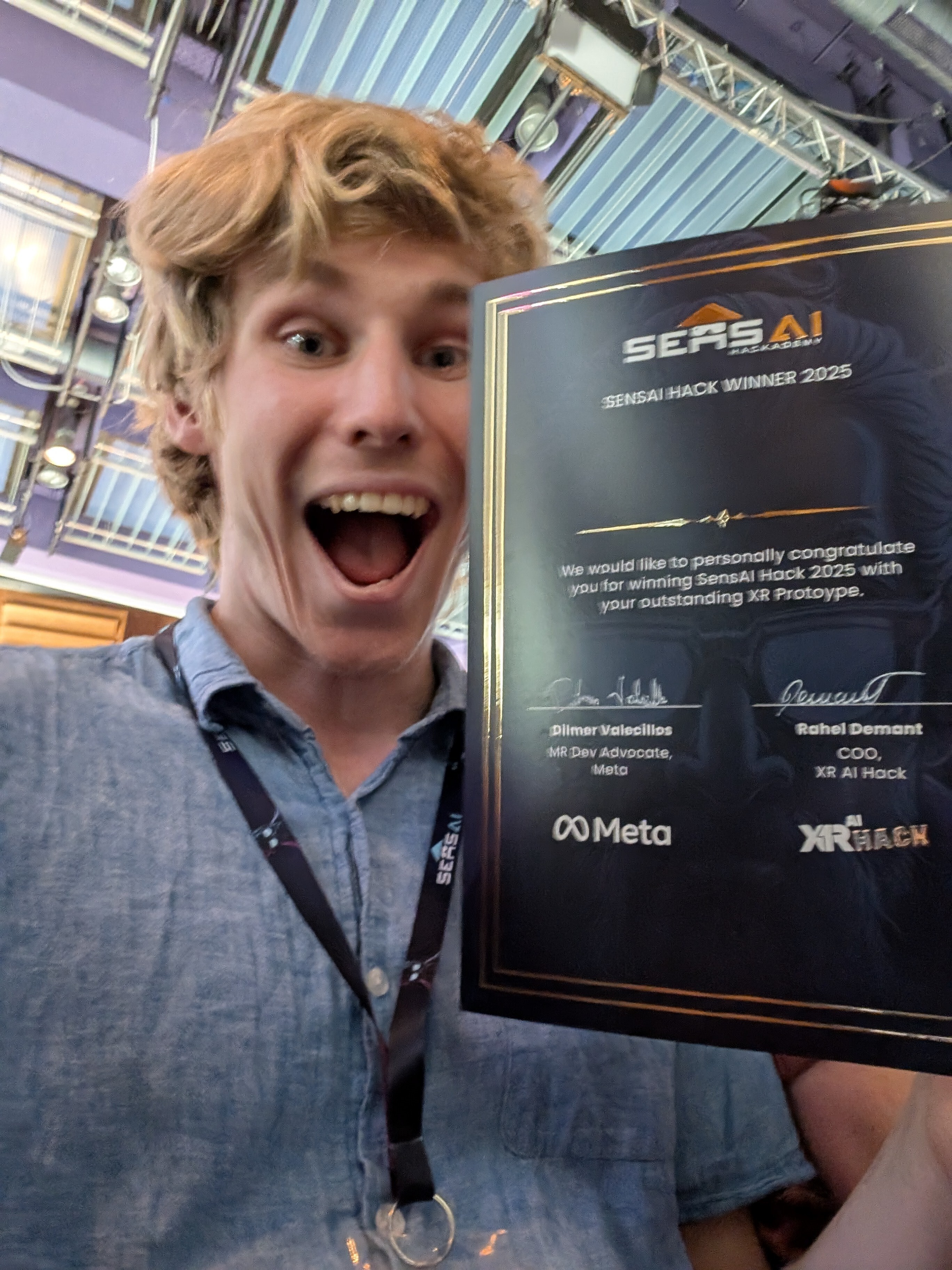 Dylan Smit kijkt blij in de camera na het winnen van zijn prijs, hij toont een embleem met 'Sensai Hack 2025'